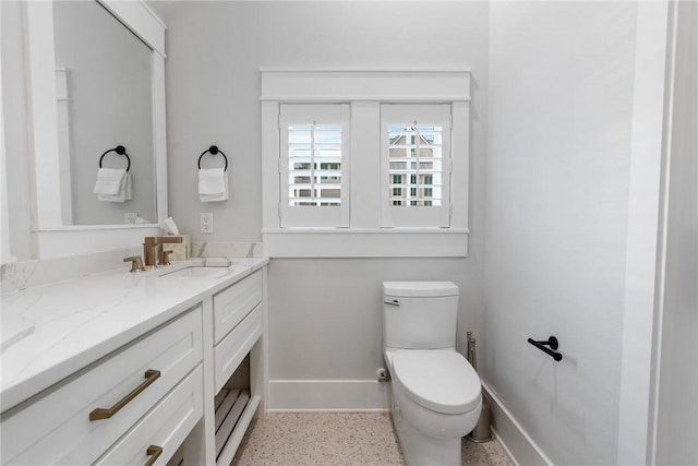 half bath with vanity, toilet, speckled floor, and baseboards