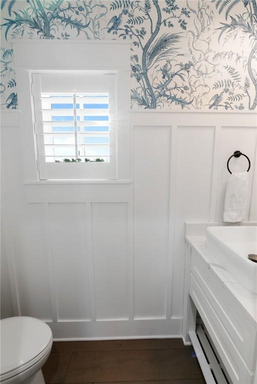 bathroom with a wainscoted wall, toilet, vanity, and a decorative wall