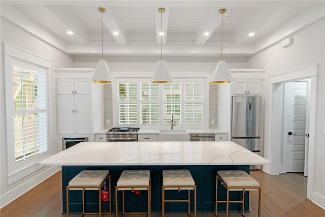 kitchen featuring light wood finished floors, beamed ceiling, appliances with stainless steel finishes, white cabinets, and a sink