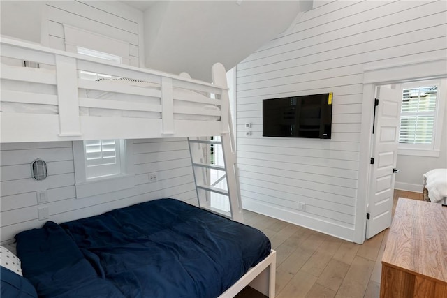 bedroom with baseboards, wooden walls, lofted ceiling, and light wood finished floors