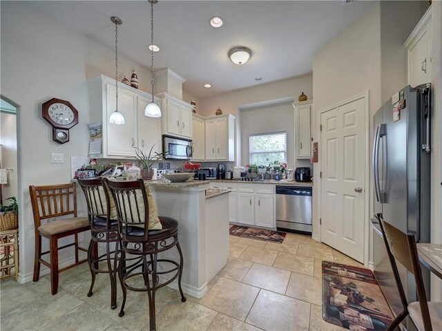 13838 Sea Horse Ave, Corpus Christi, TX 78418 - kitchen featuring appliances with stainless steel finishes, a peninsula, white cabinets, decorative light fixtures, and a kitchen bar