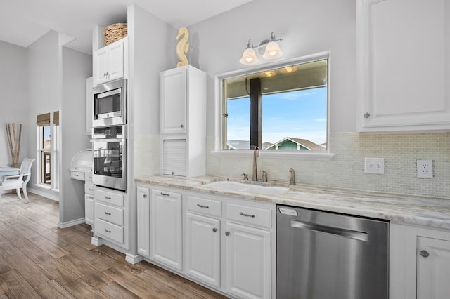 kitchen with stainless steel appliances, a sink, white cabinetry, light stone countertops, and light wood finished floors