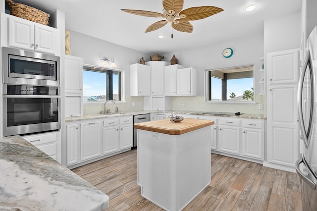 kitchen featuring light stone counters, stainless steel appliances, a sink, white cabinets, and a center island