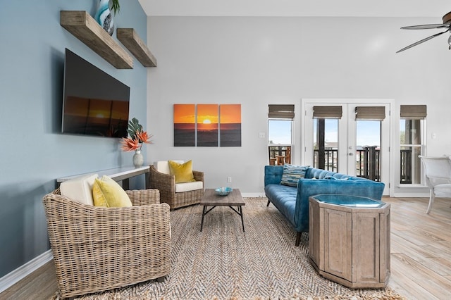 living room with a ceiling fan, french doors, light wood-style floors, and a high ceiling