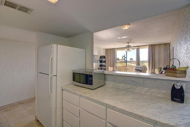 kitchen with white cabinets, white fridge, light tile patterned floors, ceiling fan, and light stone counters