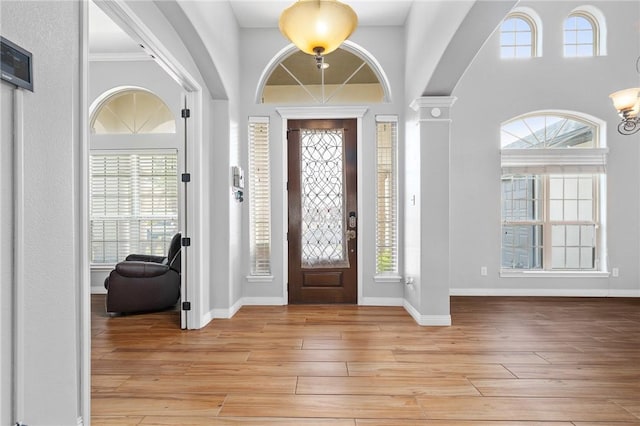 entrance foyer with decorative columns, a wealth of natural light, ornamental molding, and light hardwood / wood-style floors