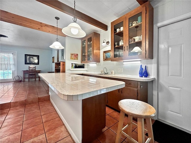 kitchen featuring tile patterned flooring, tile counters, hanging light fixtures, beam ceiling, and sink