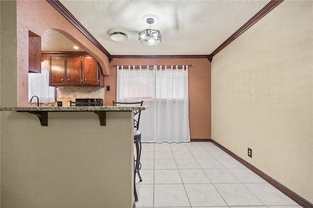 1317 Easthaven Dr, Corpus Christi, TX 78412 - kitchen featuring crown molding, a kitchen bar, dark stone countertops, a peninsula, and a textured ceiling