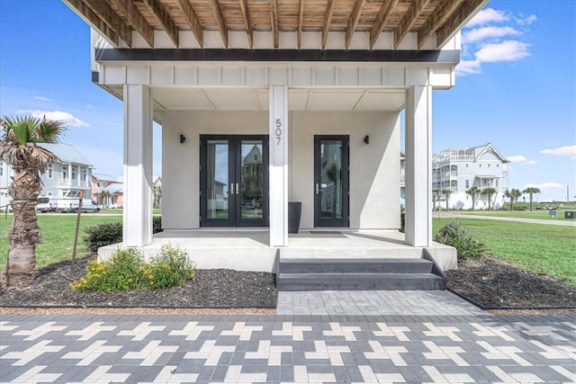 doorway to property with a yard, french doors, covered porch, and stucco siding