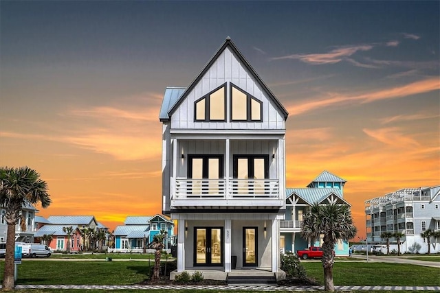 view of front of home with a front yard, a balcony, board and batten siding, and french doors