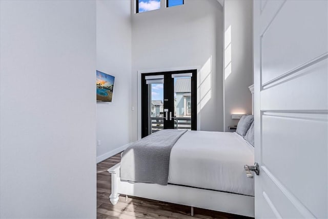 bedroom featuring access to exterior, baseboards, a high ceiling, and wood finished floors