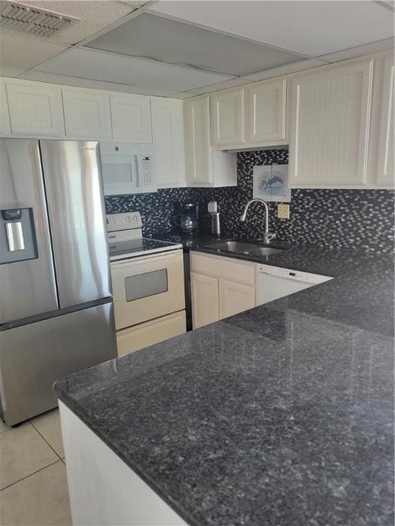 kitchen with white appliances, dark stone counters, light tile patterned flooring, a sink, and backsplash