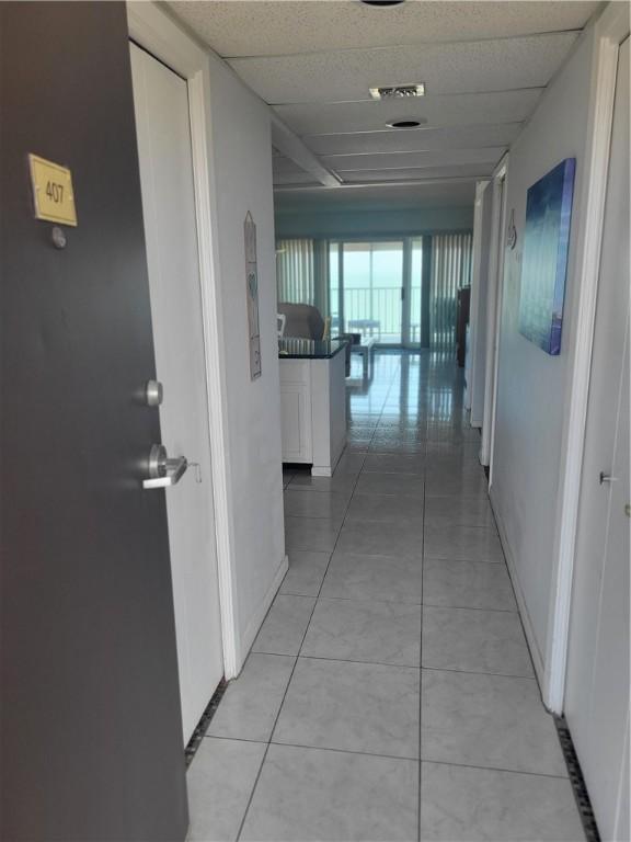 corridor featuring light tile patterned floors, baseboards, and a paneled ceiling