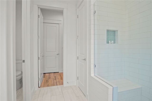 bathroom with wood-type flooring, toilet, and tiled shower