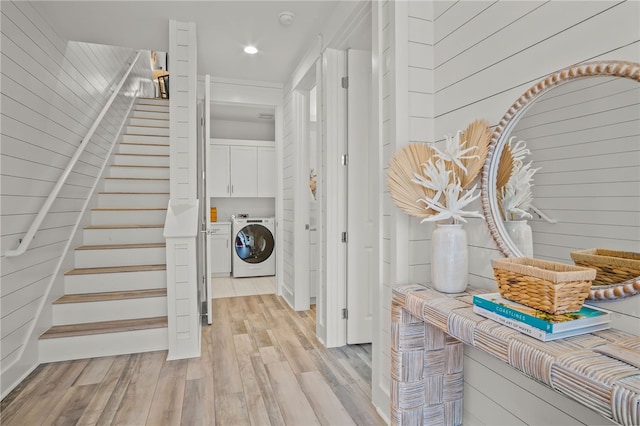 laundry area featuring separate washer and dryer, wood walls, cabinets, and light hardwood / wood-style floors