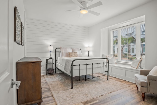 bedroom featuring wood walls, wood-type flooring, and ceiling fan