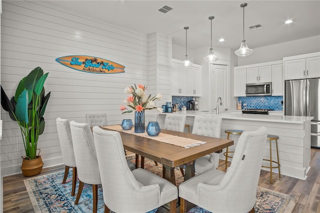 dining area with dark hardwood / wood-style flooring, wood walls, and sink