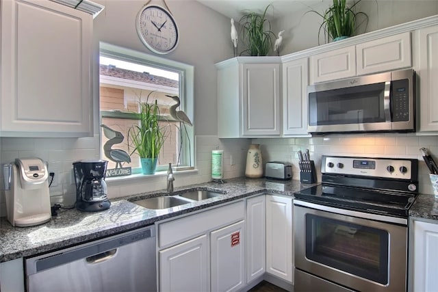 kitchen featuring sink, appliances with stainless steel finishes, white cabinetry, dark stone countertops, and decorative backsplash