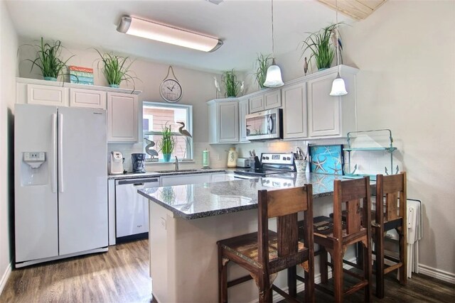 kitchen with dark stone countertops, hanging light fixtures, stainless steel appliances, a kitchen bar, and kitchen peninsula