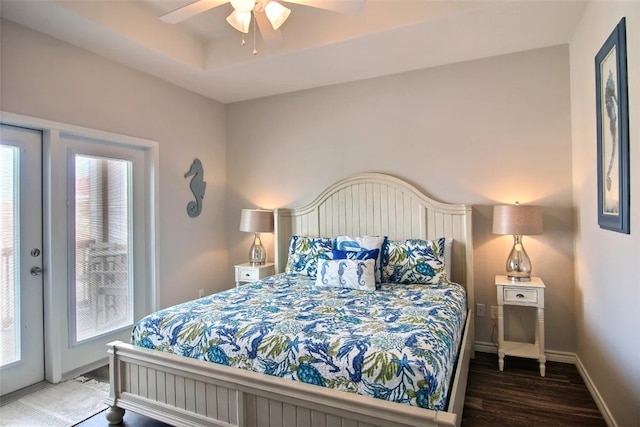 bedroom with ceiling fan, dark hardwood / wood-style floors, a raised ceiling, and access to exterior