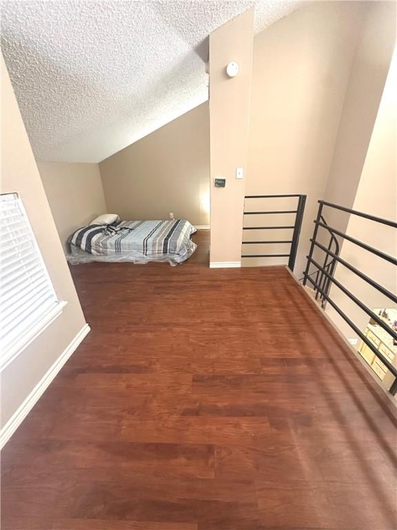 bedroom featuring vaulted ceiling, dark wood-type flooring, and a textured ceiling