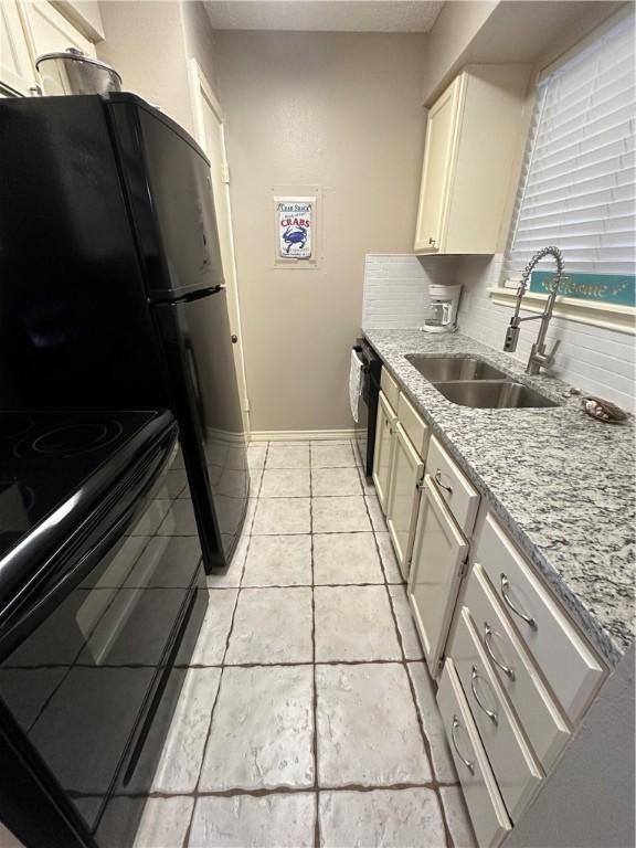 kitchen with light stone countertops, backsplash, sink, dishwasher, and black / electric stove