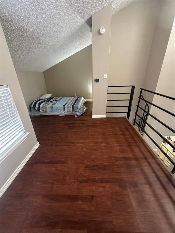 bedroom featuring dark hardwood / wood-style flooring, lofted ceiling, and a textured ceiling