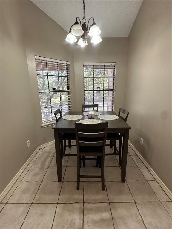 tiled dining room with a notable chandelier, a textured ceiling, and vaulted ceiling