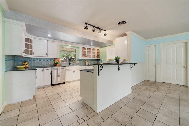 kitchen featuring a peninsula, white cabinets, stainless steel dishwasher, dark countertops, and glass insert cabinets