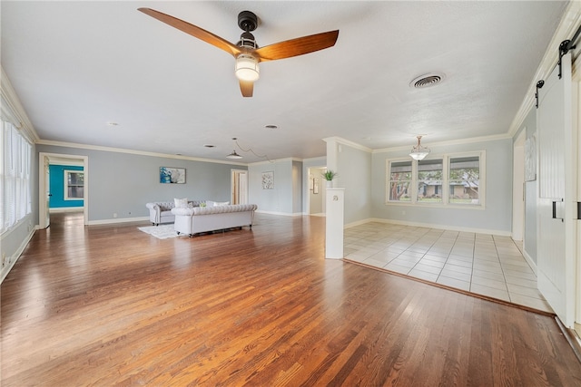 unfurnished living room featuring ornamental molding, a barn door, light wood-style flooring, and baseboards