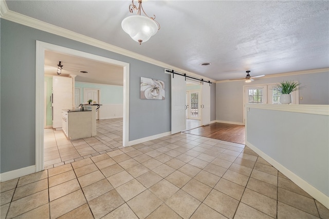 empty room featuring a textured ceiling, a barn door, light tile patterned flooring, and crown molding