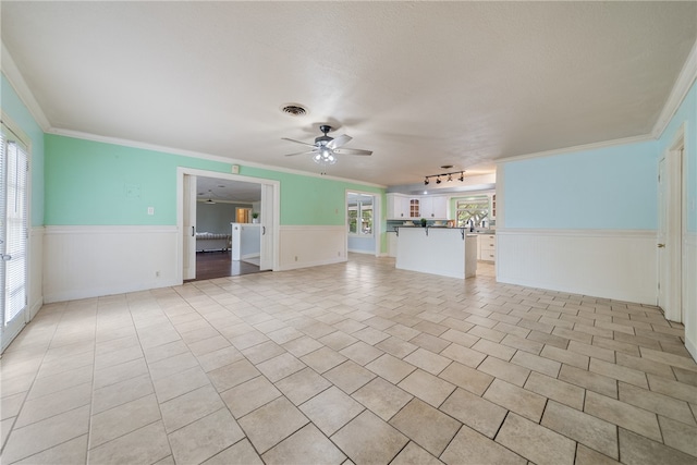 unfurnished living room with a wainscoted wall, ornamental molding, and a ceiling fan