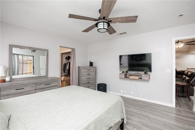 bedroom with a spacious closet, wood-type flooring, a closet, and ceiling fan