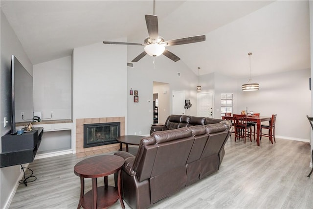 living room featuring a tile fireplace, vaulted ceiling, ceiling fan, and light hardwood / wood-style flooring