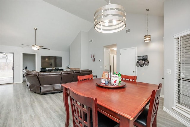 dining space featuring ceiling fan with notable chandelier, light hardwood / wood-style flooring, and high vaulted ceiling