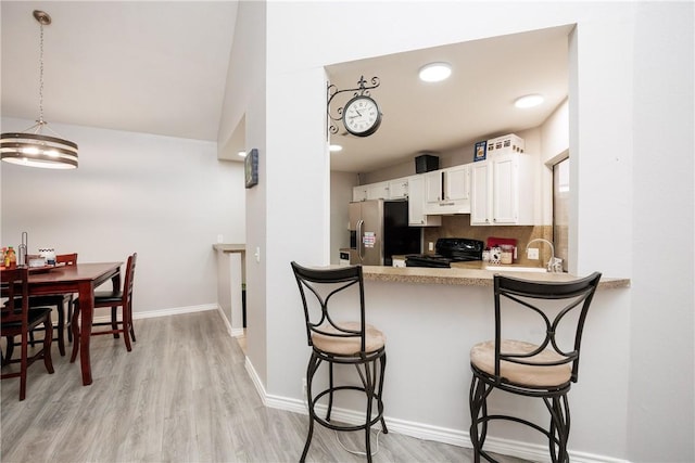 kitchen with pendant lighting, white cabinetry, a kitchen breakfast bar, stainless steel refrigerator with ice dispenser, and black / electric stove