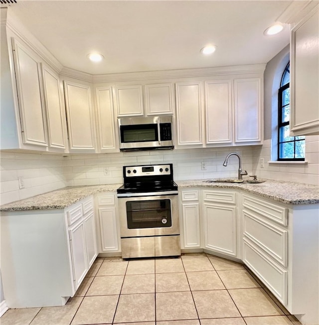 kitchen with sink, light tile patterned floors, light stone counters, white cabinets, and appliances with stainless steel finishes