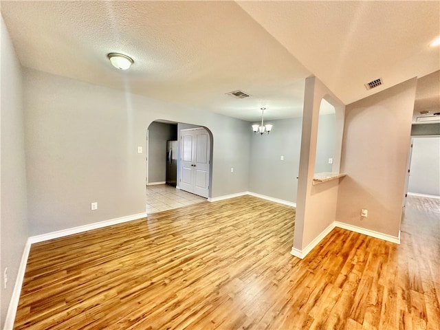 empty room with an inviting chandelier, a textured ceiling, and light hardwood / wood-style flooring