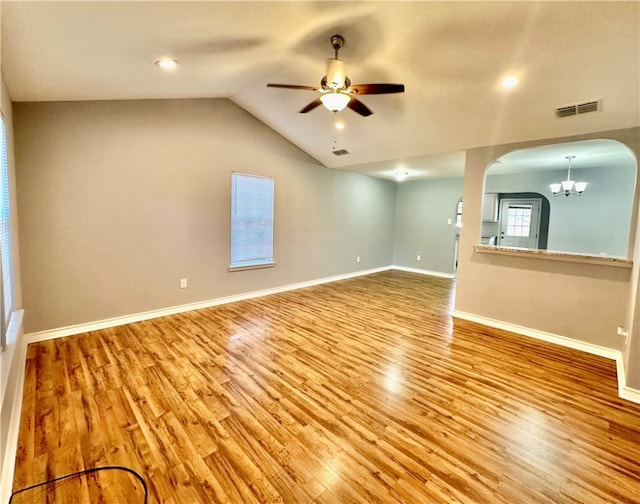 spare room with ceiling fan with notable chandelier, light hardwood / wood-style floors, and lofted ceiling