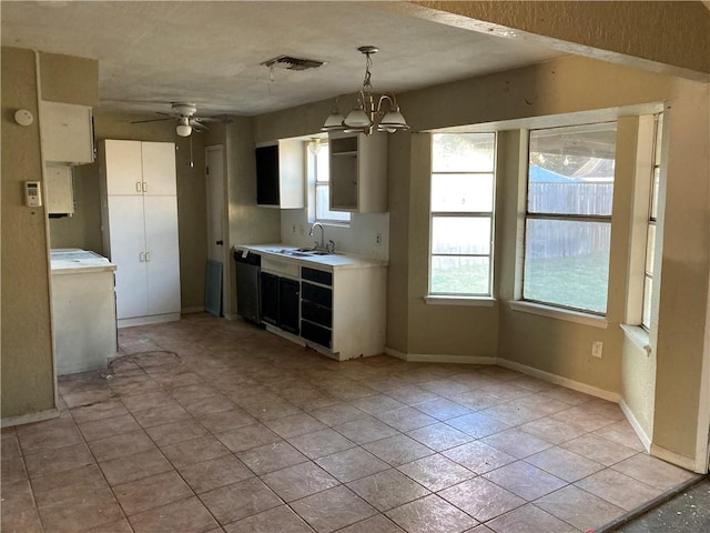 kitchen with light tile patterned floors, stainless steel dishwasher, pendant lighting, ceiling fan with notable chandelier, and sink