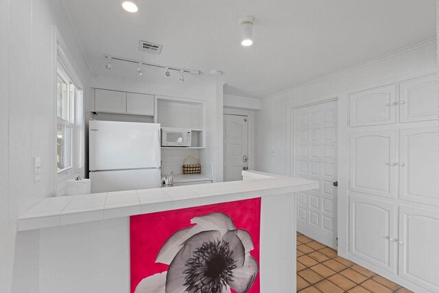 13 Sandpiper Ln, Rockport, TX 78382 - kitchen featuring white appliances, tile countertops, light tile patterned floors, a peninsula, and white cabinetry