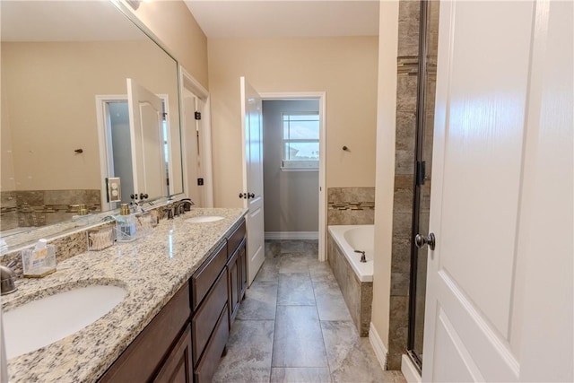 full bath with a sink, baseboards, double vanity, and a relaxing tiled tub