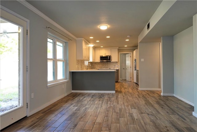 kitchen with white cabinets, kitchen peninsula, decorative backsplash, ornamental molding, and wood-type flooring