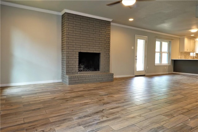 unfurnished living room with sink, ceiling fan, light wood-type flooring, a fireplace, and ornamental molding