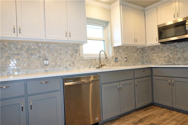 kitchen featuring tasteful backsplash, stainless steel appliances, crown molding, light hardwood / wood-style floors, and white cabinetry