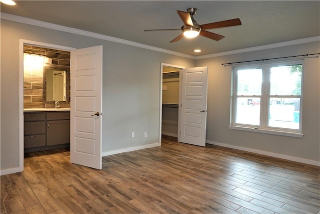 unfurnished bedroom featuring a walk in closet, crown molding, sink, ceiling fan, and wood-type flooring