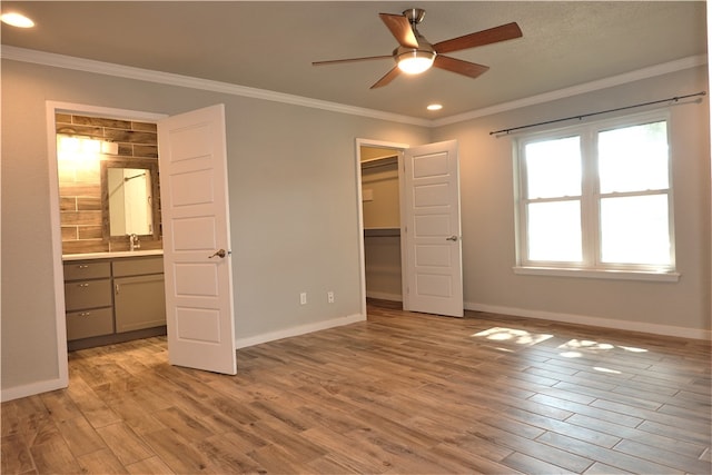 unfurnished bedroom with a walk in closet, ceiling fan, crown molding, light hardwood / wood-style flooring, and connected bathroom