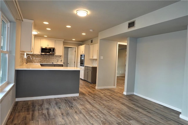 kitchen featuring sink, dark wood-type flooring, kitchen peninsula, white cabinets, and appliances with stainless steel finishes