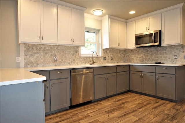 kitchen featuring gray cabinetry, white cabinetry, tasteful backsplash, light hardwood / wood-style floors, and appliances with stainless steel finishes