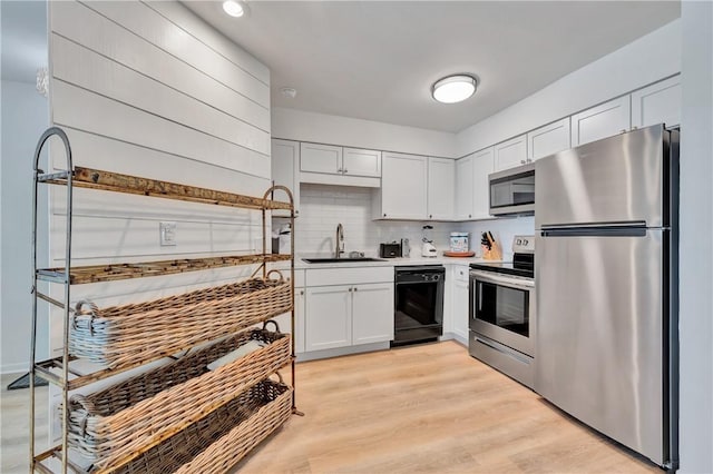 kitchen featuring sink, stainless steel appliances, tasteful backsplash, white cabinets, and light wood-type flooring